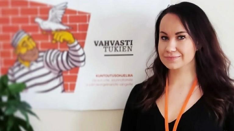 Nainen hymyilee Vahvasti tukien- kuntoutuksen julisteen edessä.